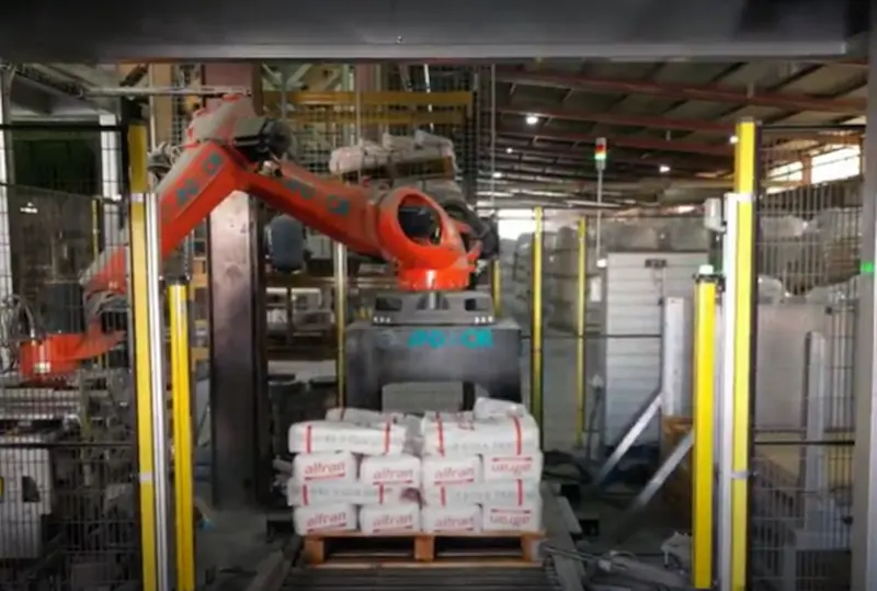 Robot industrial manipulando sacos de hormigón refractario en planta automatizada